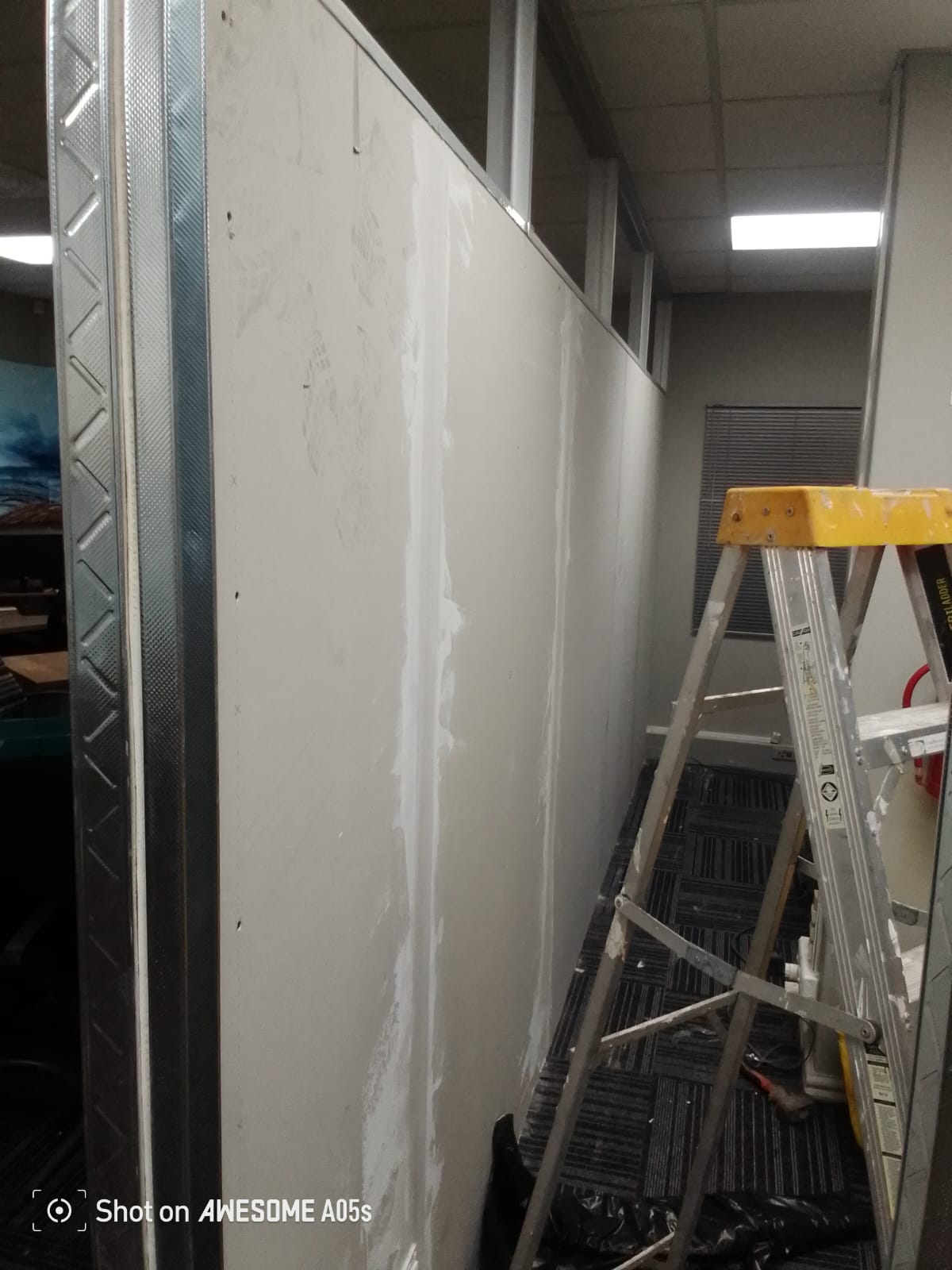 Drywall partition with seam tape mid-skim and ladder on site